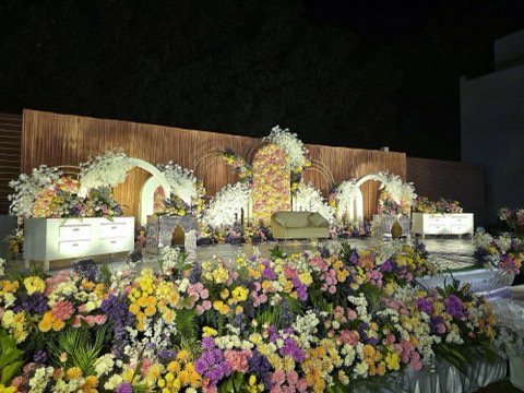 White floral stage with wooden backdrop and flower beds on the lawn