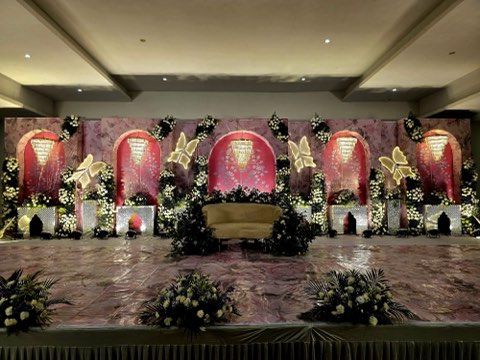 Maroon arched reception stage with chandeliers and butterfly accents at Jaithri Grand Convention